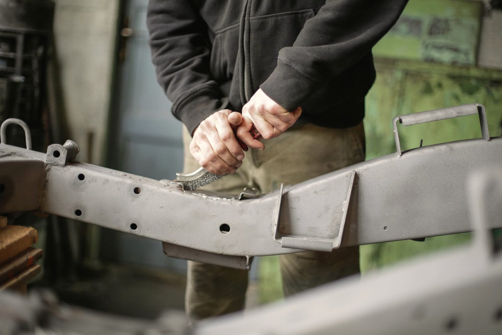 Hands working along the edge of a steel bracket at a bench.