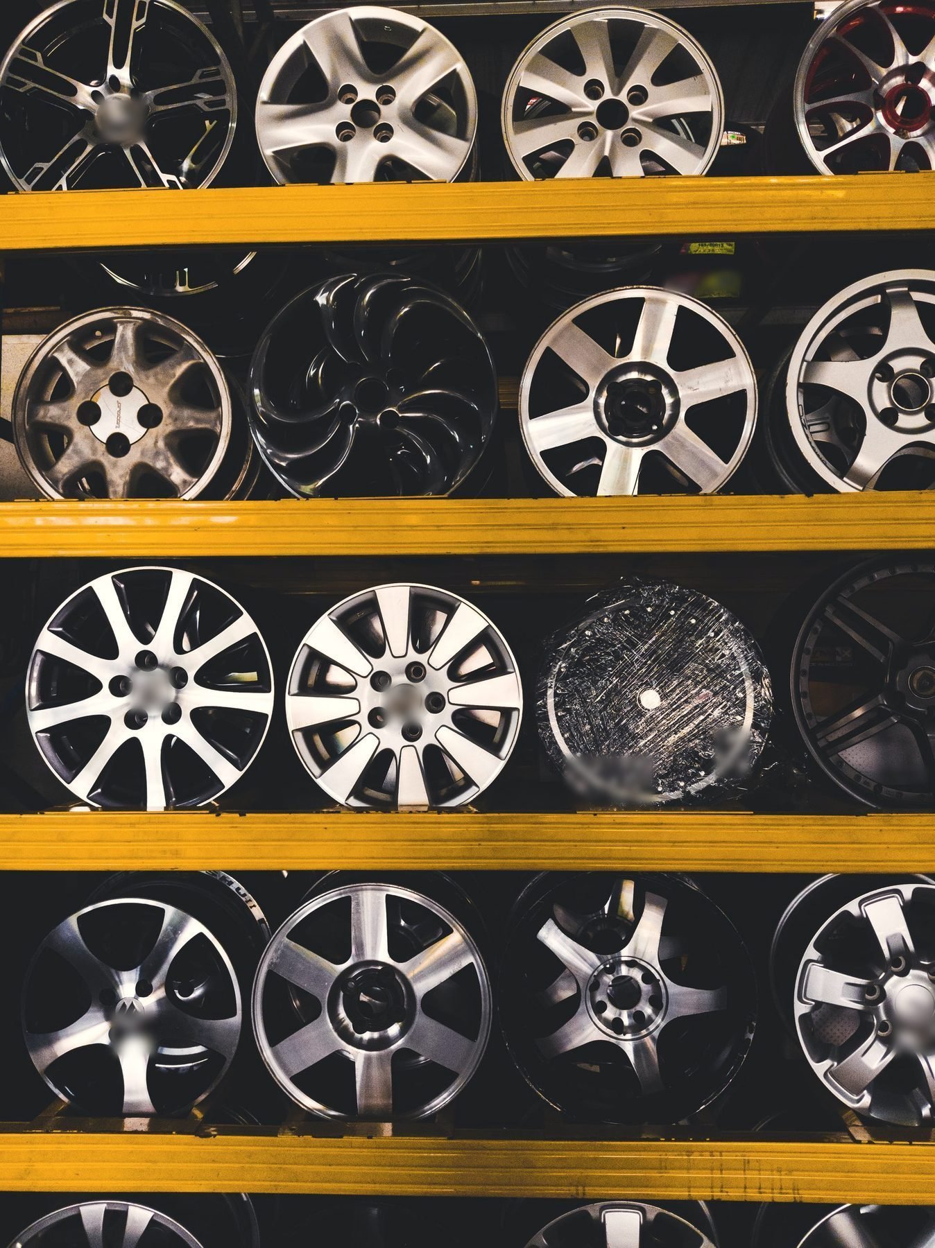 Bare alloy rims stacked in rows on yellow steel shelving.